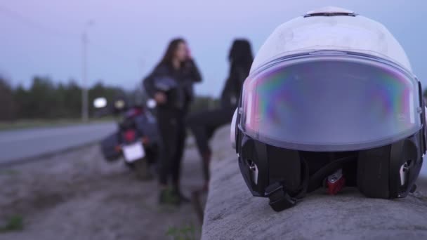 Motorcycle helmet at foreground, girls bikers relaxing after trip at background — Stock Video