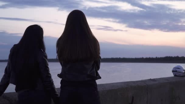 Dos moteros niñas en chaquetas de cuero disfrutan de una hermosa vista de la noche en el mar — Vídeos de Stock