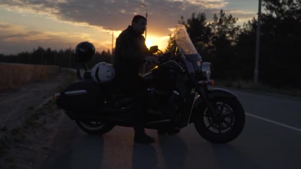 Байкер сидит на мотоцикле на фоне заката — стоковое видео