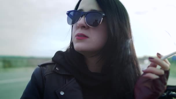 Курит женщина-байкер в солнцезащитных очках и кожаной куртке — стоковое видео