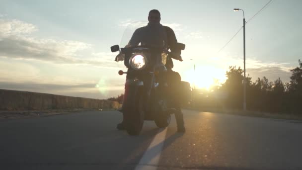 Biker op motorfiets bij zonsondergang achtergrond op de weg — Stockvideo