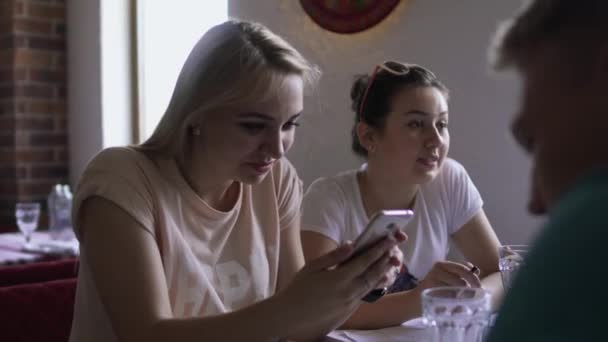 Jeune fille en utilisant le téléphone à la table dans le café et de communiquer avec des amis — Video