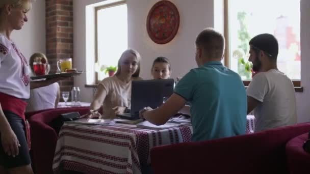 Garçonete traz bebidas para a companhia de pessoas que estudam no café — Vídeo de Stock