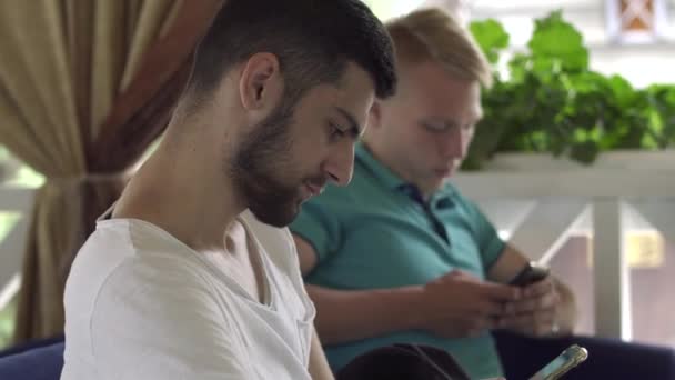 Deux jeunes hommes regardant sur l'écran de téléphones mobiles assis dans le restaurant — Video