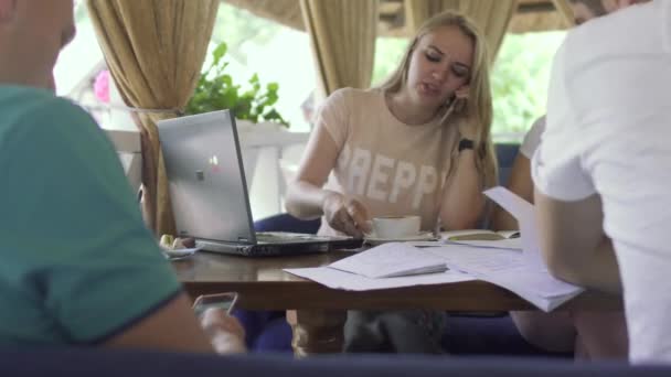 Jeune fille boire du café et parler au téléphone tout en étudiant dans un café avec des amis — Video