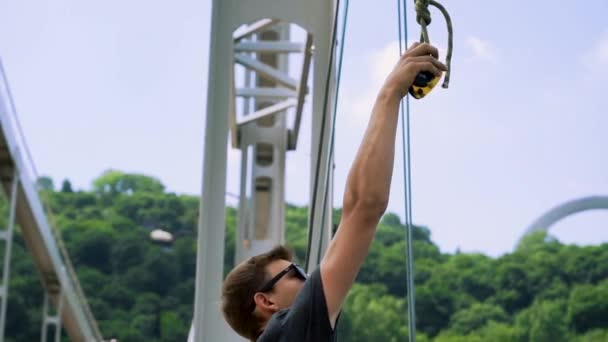 Il giovane attacca una corda a una carabina per saltare dal ponte — Video Stock