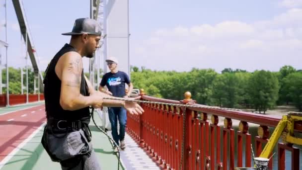 Парень в кепке на мосту тянет веревку — стоковое видео