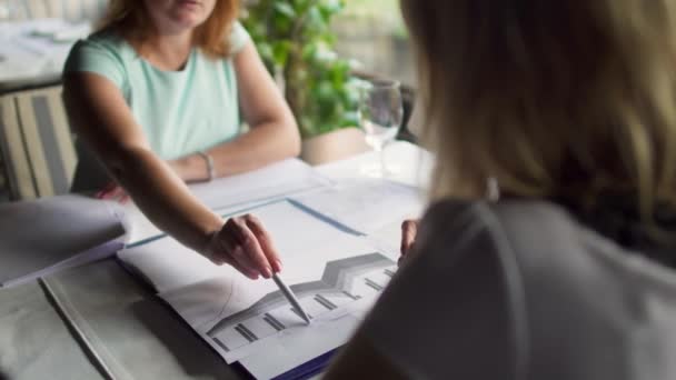 Twee volwassen vrouwen hebben een zakelijke bijeenkomst en werken met papieren in restaurant — Stockvideo