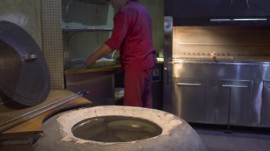 Cook kırmızı üniformalı hamur geleneksel yuvarlak soba içinde parça koyar. Adam restoranda özel yemek hazırlanıyor. Özbek kil fırında mutfak gıda hazırlama.