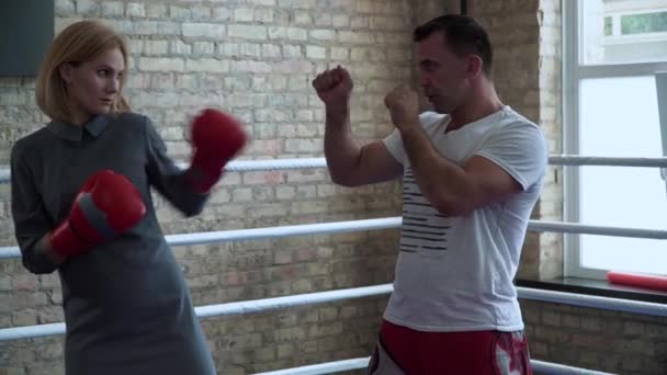 Женщина в элегантном платье, боксерские перчатки тренировка на ринге бокса с тренером — стоковое видео