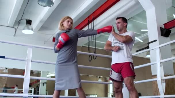 Mujer bonita en vestido y guantes de boxeo de entrenamiento con entrenador en el ring de boxeo — Vídeos de Stock