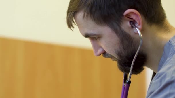 Молодой бородатый врач слушает сердцебиение пациента стетоскопом — стоковое видео