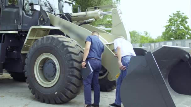 Buyer inspects tractor in outdoors showroom and talks with manager — Stock Video