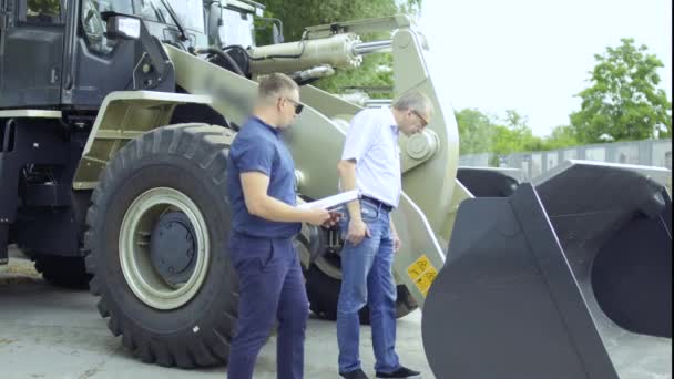 Farmer talks with salesman about tractor with scoop — Stock Video