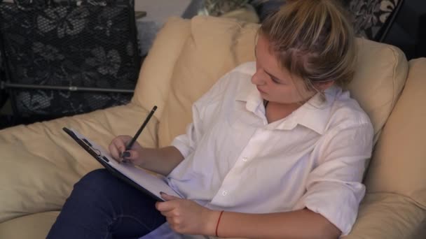 Charming young lady writes sitting in a leather armchair — Stock Video