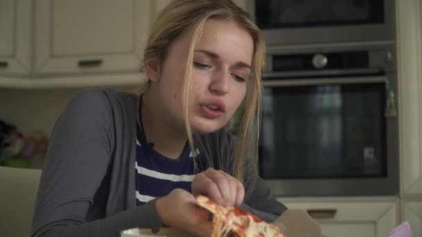 Schöne Blondine isst Pizza in der Küche — Stockvideo