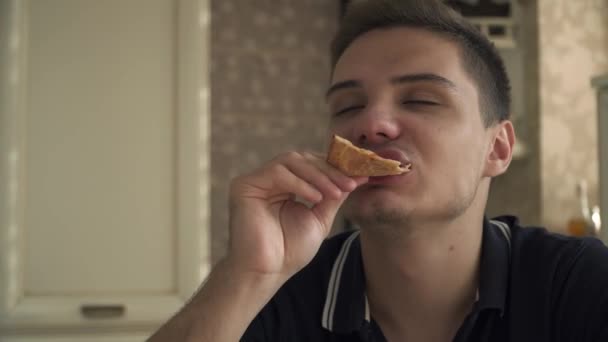 Guapo chico comer pizza en la cocina y disfrutando de ella — Vídeos de Stock