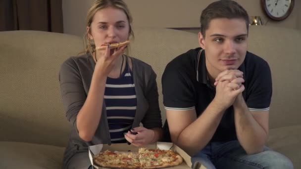 Pareja joven con una caja de pizza se sienta en el sofá — Vídeo de stock