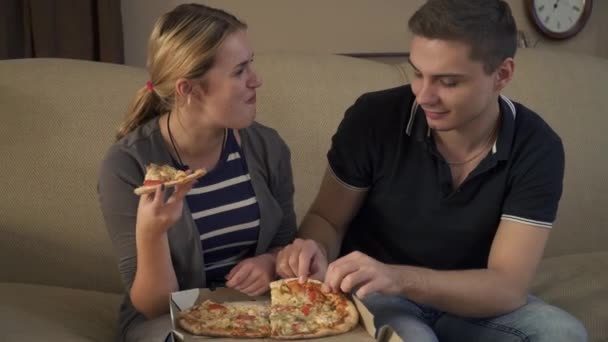 Красивая молодая пара сидит на диване и ест пиццу — стоковое видео