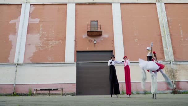 Två komiska par på styltor dansar nära byggnaden — Stockvideo