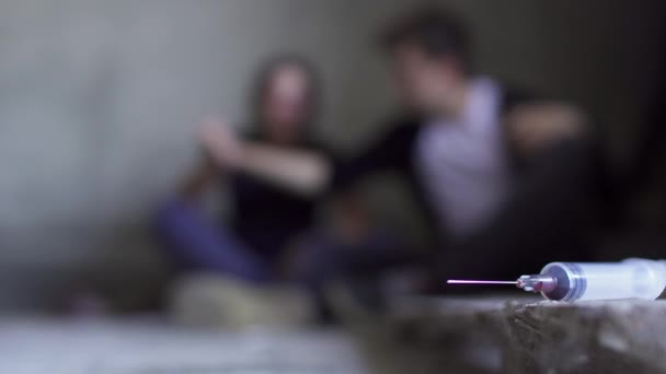 Двоє людей сидять на підлозі на фоні використаного шприца — стокове відео
