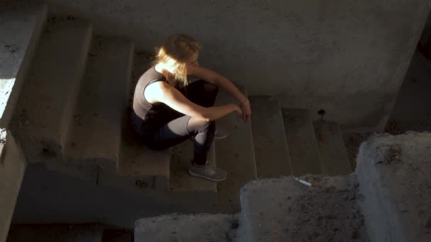 Untidy girl is sitting at the stairs in an abandoned building — Stock Video