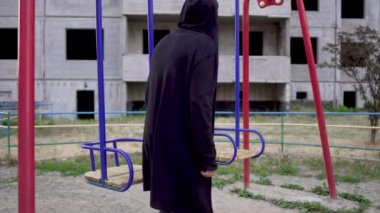 Kötü görünümlü çocuk gelir ve salıncağa oturur