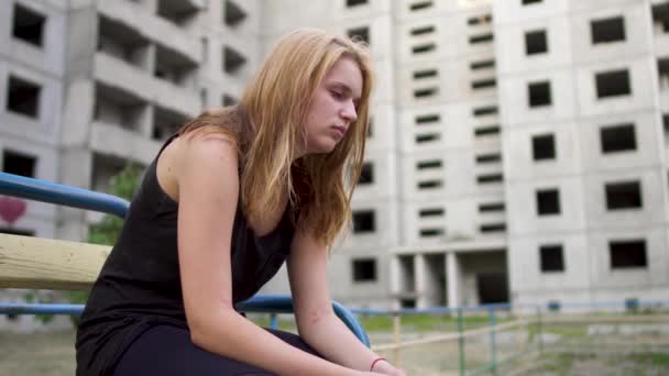 Девушка сидит возле заброшенного здания — стоковое видео
