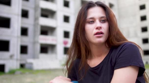 Nervöses brünettes Mädchen sitzt in der Nähe eines hohen Gebäudes — Stockvideo