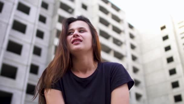 Сумасшедшая брюнетка сидит рядом с высоким зданием — стоковое видео