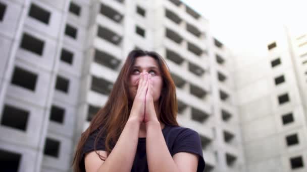 Menina olhando louco está sentado perto de edifício alto e orando para o céu — Vídeo de Stock