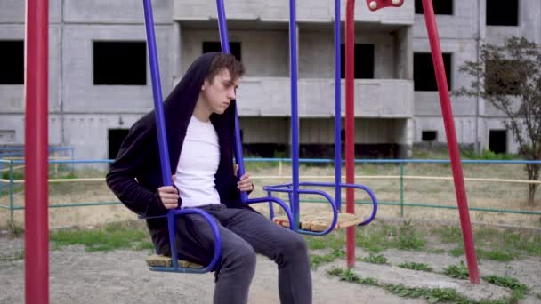 Молодой человек в плохом состоянии здоровья сидит на качелях — стоковое видео