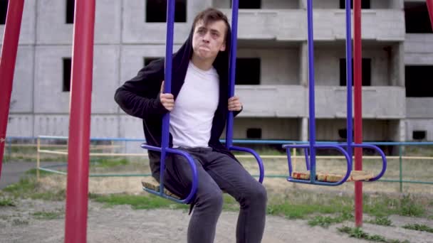 Junger Mann in schlechtem Gesundheitszustand sitzt auf einer Schaukel — Stockvideo