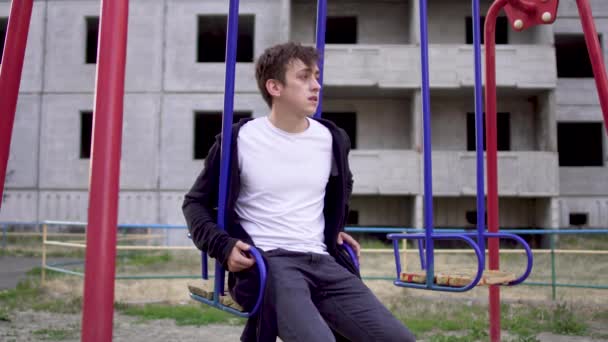 Молодой человек в плохом состоянии здоровья сидит на качелях — стоковое видео