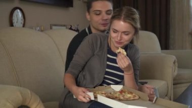 Kanepede oturan ve pizza yemek çekici genç çift