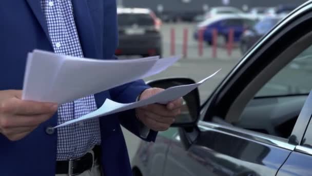 Бизнесмен стоит у машины и просматривает деловые документы. — стоковое видео