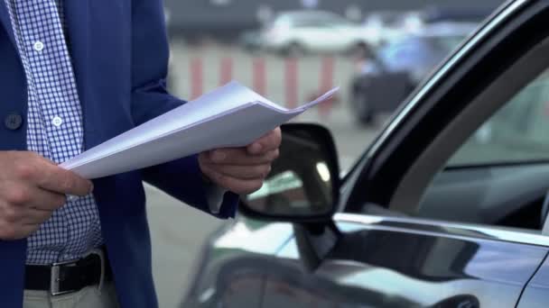Empresario está de pie junto al coche y mirando a través de los documentos de negocios — Vídeos de Stock