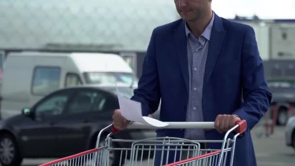 Zakenman met handelspapieren staat in de buurt van een trolley — Stockvideo