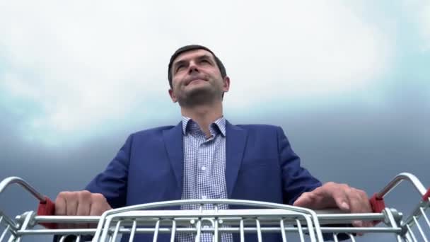 Schöner Mann trägt einen Einkaufswagen auf dem Parkplatz in der Nähe des Supermarktes — Stockvideo