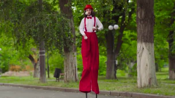 Grappige jonge mime loopt op stelten en jongleren — Stockvideo