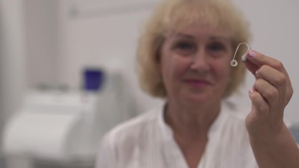 Adult woman holds a hearing aid in front of the camera — Stock Video