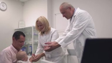 Babası hastanede bebekle. Doktor ve hemşire çocuğun eline işaret.