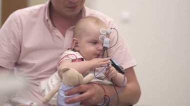 Babam elindeki hastanede tıbbi sensörleri ile bir bebek tutan. Doktorlar muayene bebeğe. Yaş Bebek bir oyuncak tutuyor. Doktor bebeğin için sensörler ayarlar.
