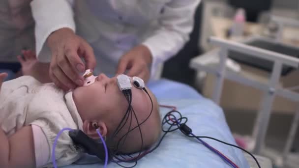 Criança com uma chupeta na boca e sensores médicos na cabeça — Vídeo de Stock