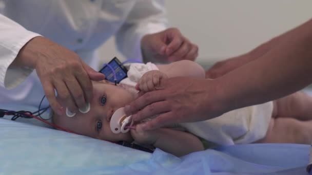 Hermoso bebé se encuentra con sensores médicos en una mesa en el hospital . — Vídeo de stock