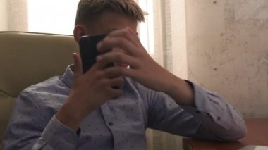 Yakışıklı çocuk bir sandalyede oturuyor ve telefonda tıklayarak