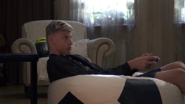 Молодой парень сидит на большом диване в своей комнате — стоковое видео