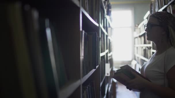 Vacker ung flicka mellan raderna med böcker i biblioteket — Stockvideo