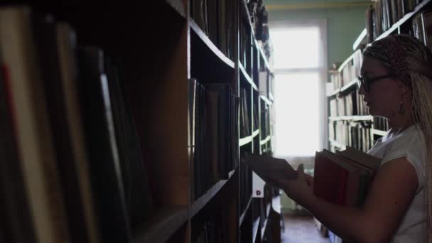 Mooie blonde tussen de rijen met boeken in de bibliotheek — Stockvideo