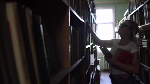 Joven rubia entre las filas con libros en la biblioteca — Vídeo de stock